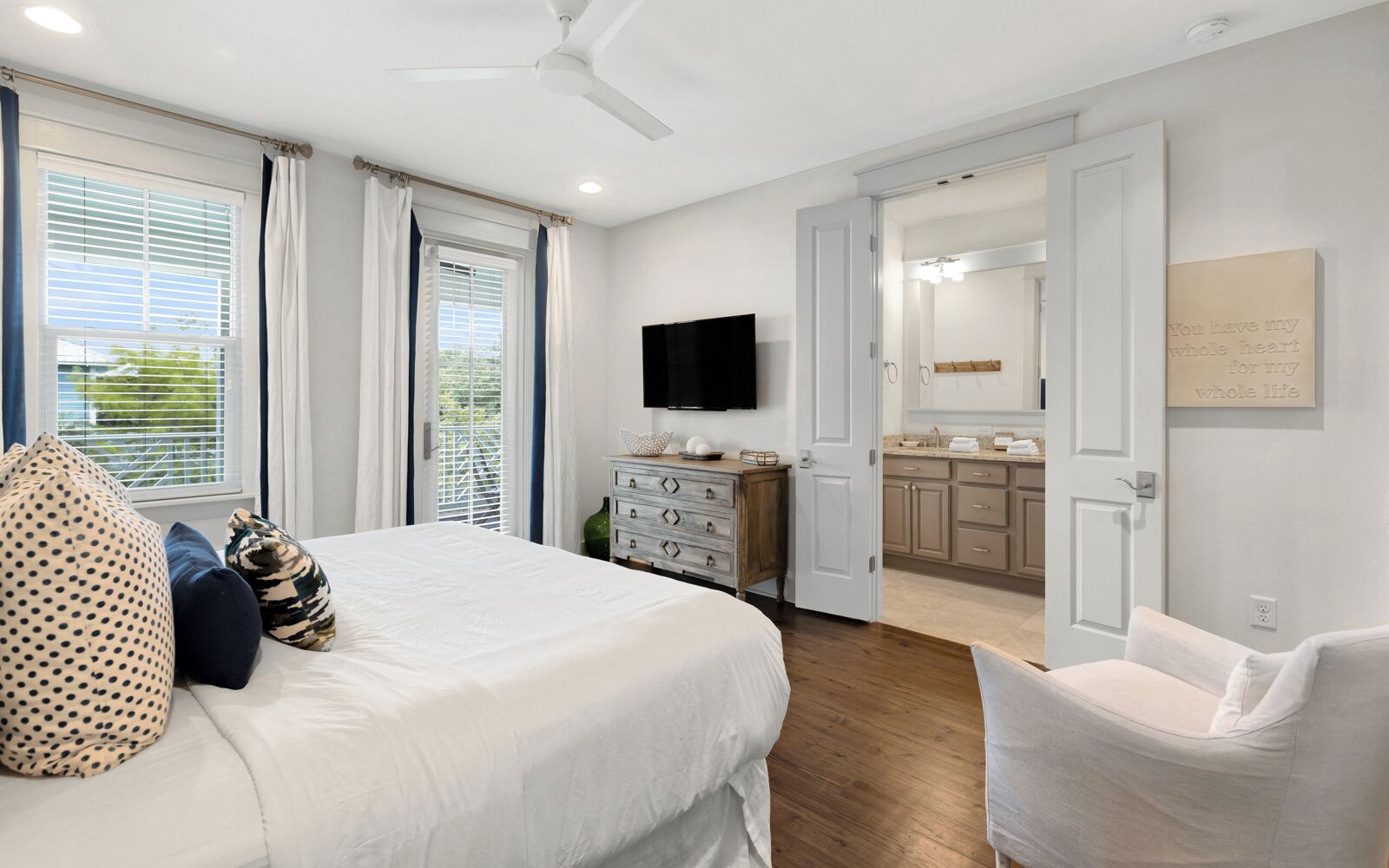 A bedroom with a bed, a dresser, a television, and a bathroom visible through an open door.