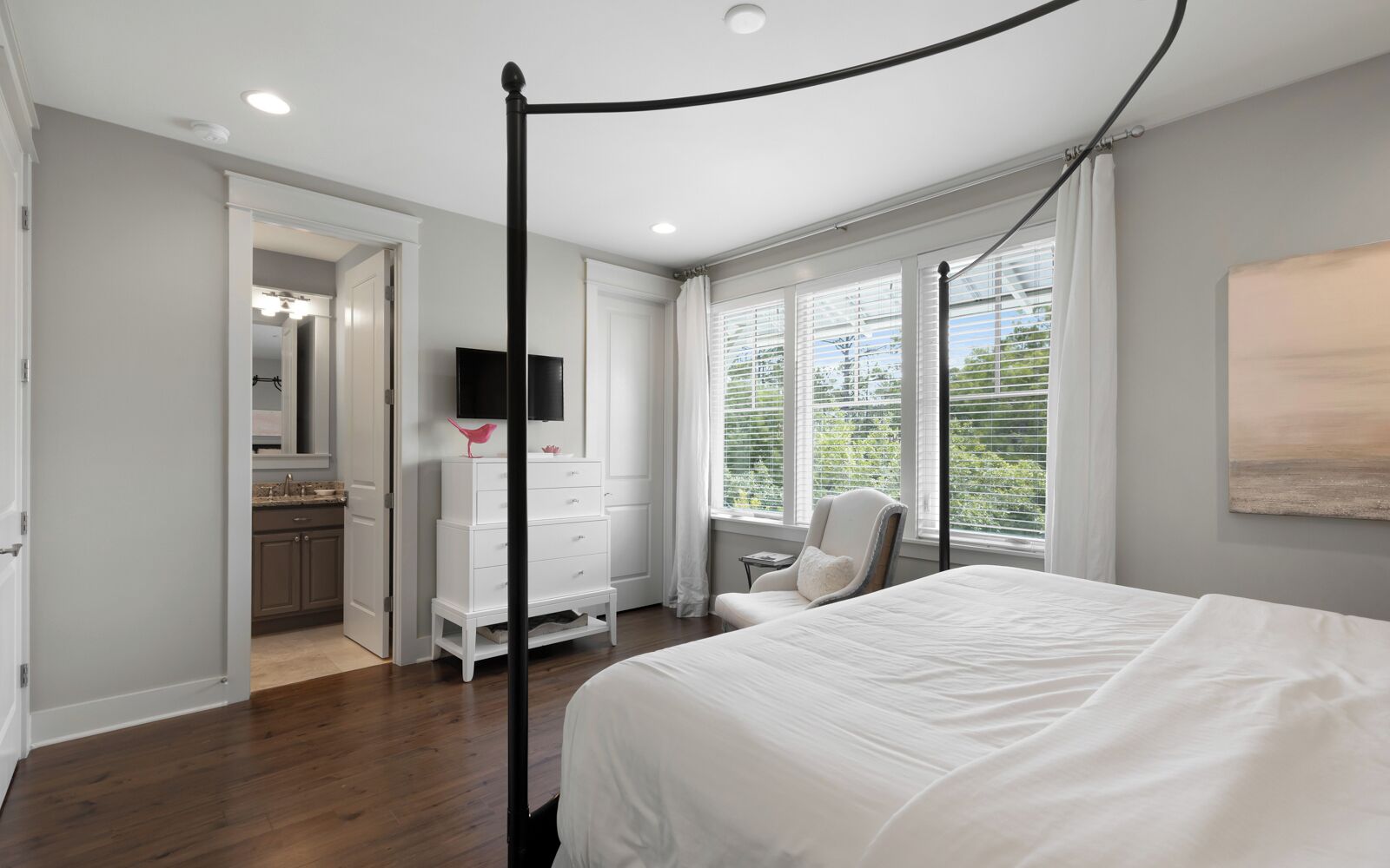 A bedroom with a four-poster bed, a dresser, a chair, and a TV mounted on the wall.