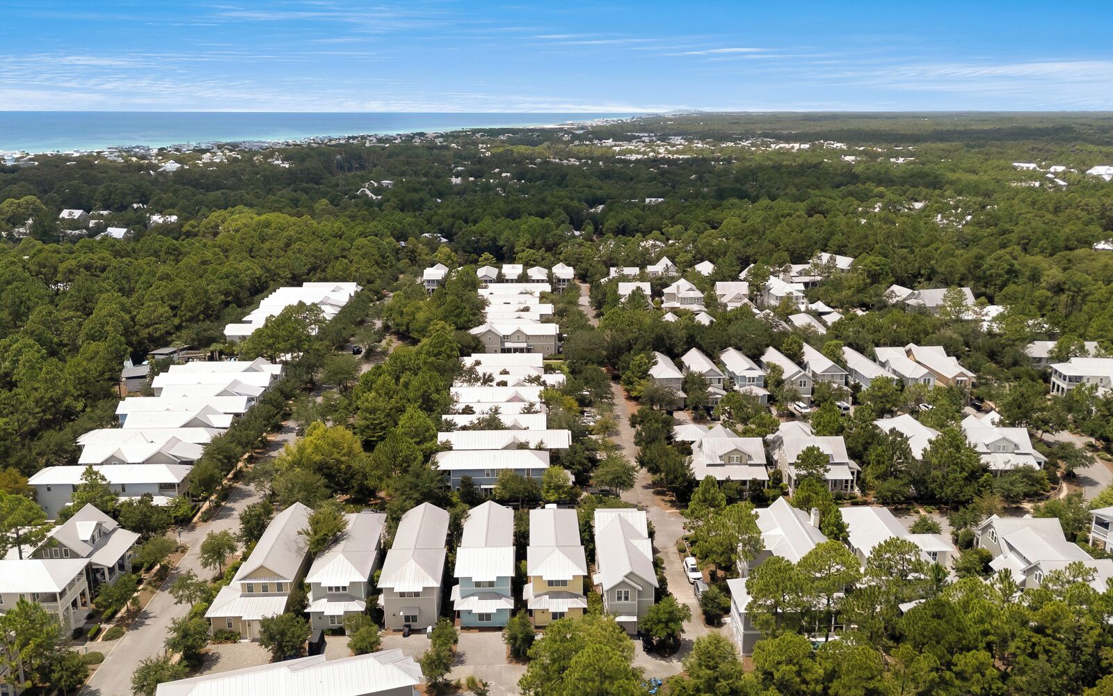 Une vue aérienne d’un quartier résidentiel avec de nombreuses maisons, entouré d’une végétation luxuriante et surplombé d’un ciel dégagé.