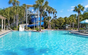 A swimming pool with a water slide and palm trees.