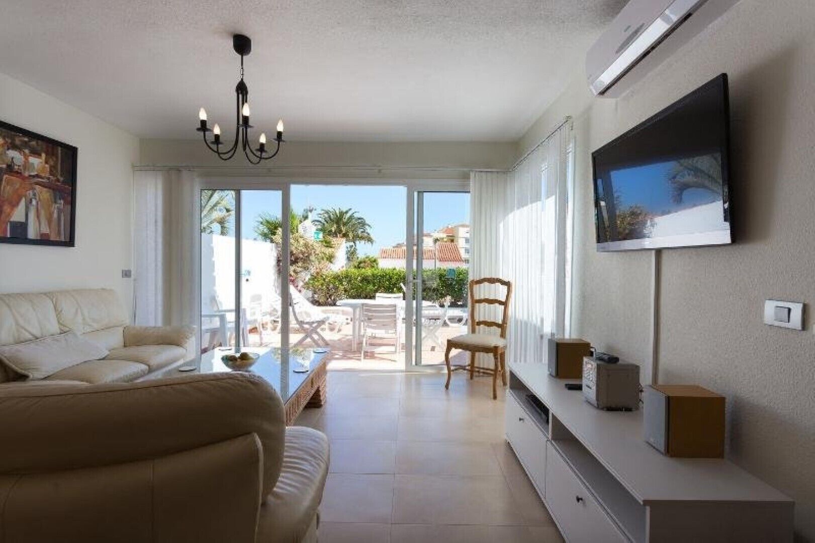 A modern living room with a sofa, a TV mounted on the wall, and a balcony with outdoor furniture.