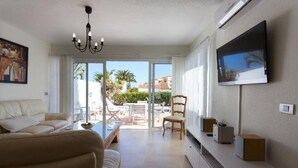 Ein modernes Wohnzimmer mit einer Couch, einem an der Wand montierten Fernseher und einem Balkon mit Gartenmöbeln.