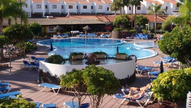 Ein Poolbereich eines Resorts mit mehreren Liegestühlen und einer zentralen Wasserspende.
