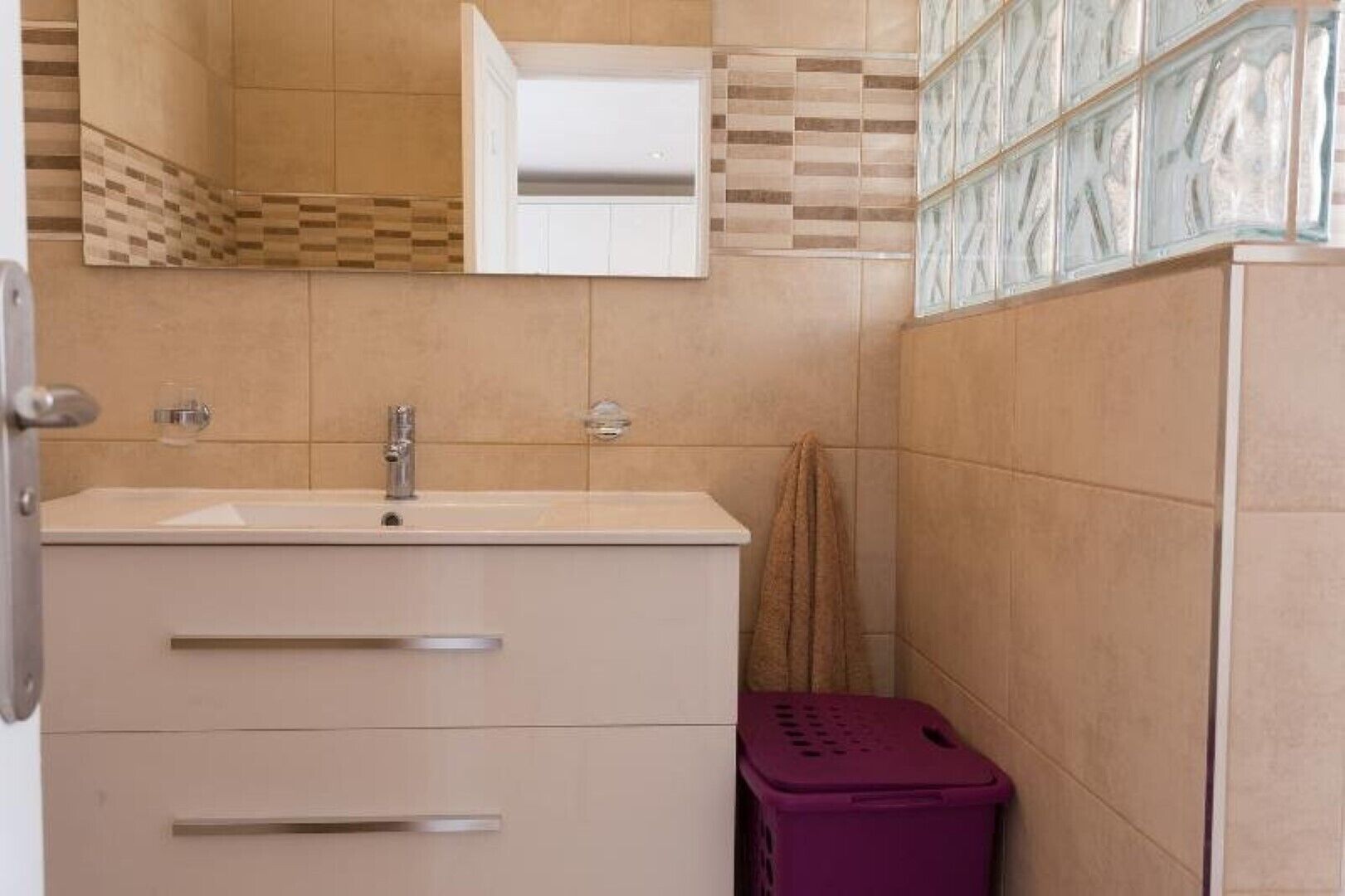 A bathroom with a sink, mirror, and a purple laundry basket.