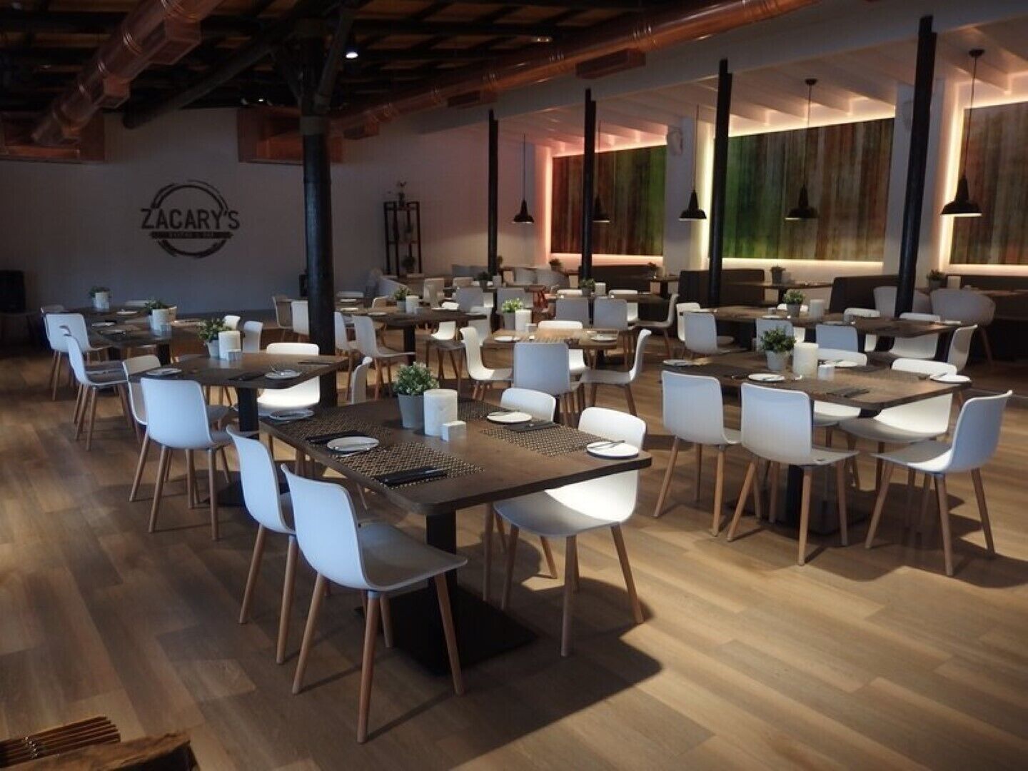 Un restaurant spacieux, doté de nombreuses tables et chaises, d’un plancher en bois et d’un éclairage suspendu.