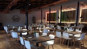 Ein geräumiges Restaurant mit mehreren Tischen und Stühlen, Holzboden und Pendelleuchten.