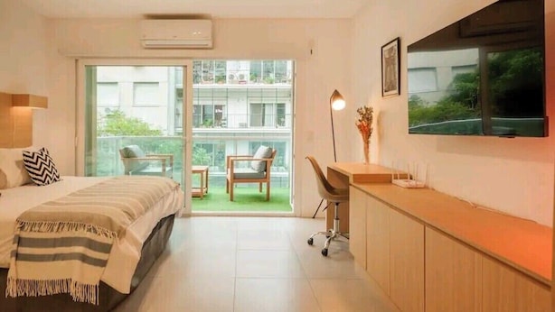 Una habitación de hotel moderna con cama, escritorio, silla, televisor y balcón con vista a la ciudad.