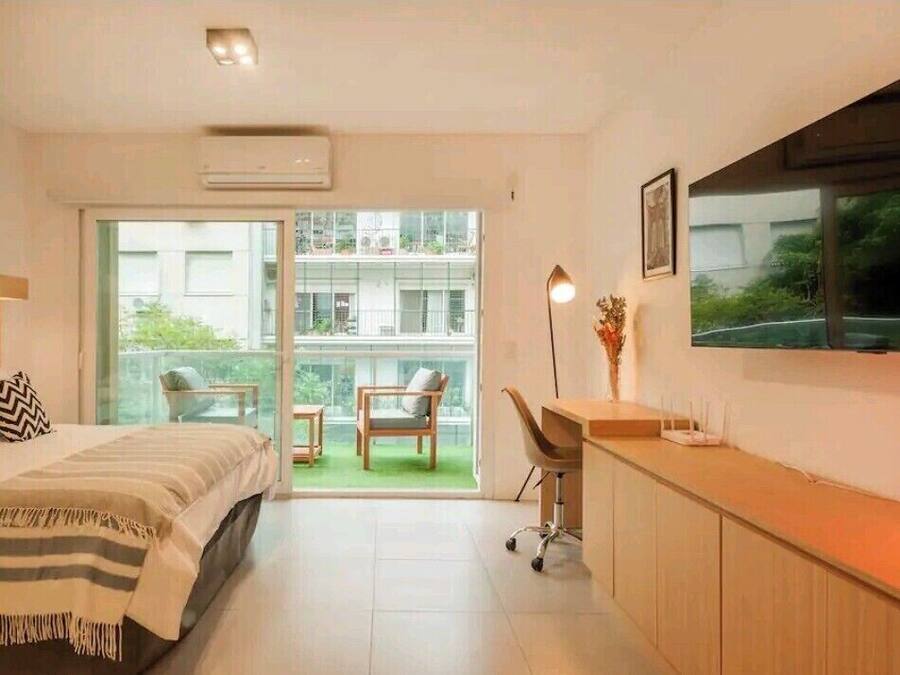 Quarto de hotel moderno com cama, escrivaninha, cadeira, TV e varanda com vista para a cidade.
