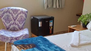 Une chambre d’hôtel avec un lit, une chaise, une petite table, un radiateur et une fenêtre avec des rideaux.