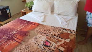 Un lit avec du linge de lit blanc, une couverture à motifs léopard et une petite table de chevet sur laquelle est posée une plante.