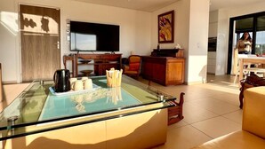 Una sala de estar moderna con una mesa de centro de vidrio, un televisor de pantalla plana y un cuadro grande en la pared.