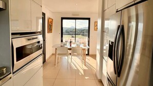 Una cocina moderna con armarios blancos, un refrigerador de acero inoxidable y una zona de comedor con mesa y sillas.
