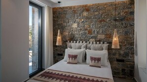 Un dormitorio con pared de piedra, una cama grande con ropa de cama blanca y dos lámparas colgantes.