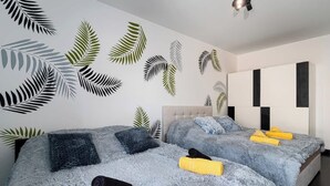 A bedroom with two beds, each with a fluffy blue blanket and pillows, and a wall decorated with large leaf patterns.