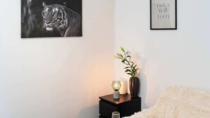 A bedroom with a white bed, a black nightstand with a vase and a lamp, a framed picture of a tiger, and a framed quote on the wall.