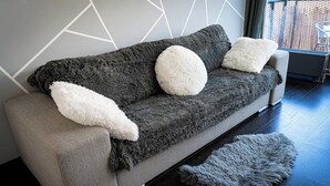A modern living room with a grey sofa, white fluffy cushions, and a grey furry rug.
