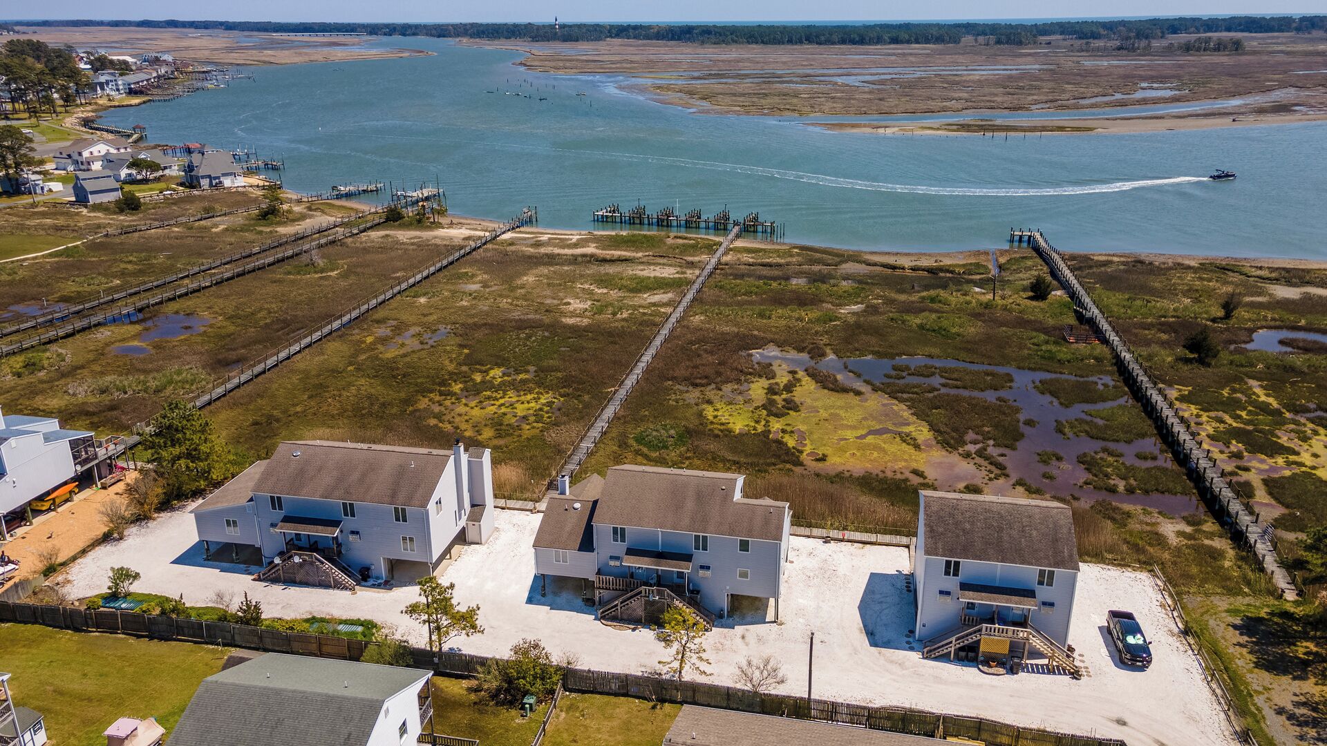 Une propriété située sur la côte, comprenant deux maisons à deux étages, un quai et une jetée s’avançant dans une vaste étendue d’eau.