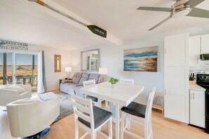 Un salon moderne avec une table à manger, des chaises blanches, un ventilateur de plafond et une vue sur l’extérieur.