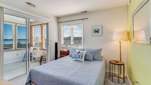 Camera da letto con un letto, una scrivania, una sedia, una lampada e vista mare attraverso ampie finestre.