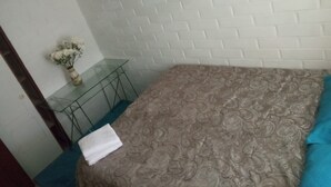 Une pièce avec une couvre-lit à motifs, une table en verre ornée d’un vase de fleurs et un mur blanc imitant un mur de briques.