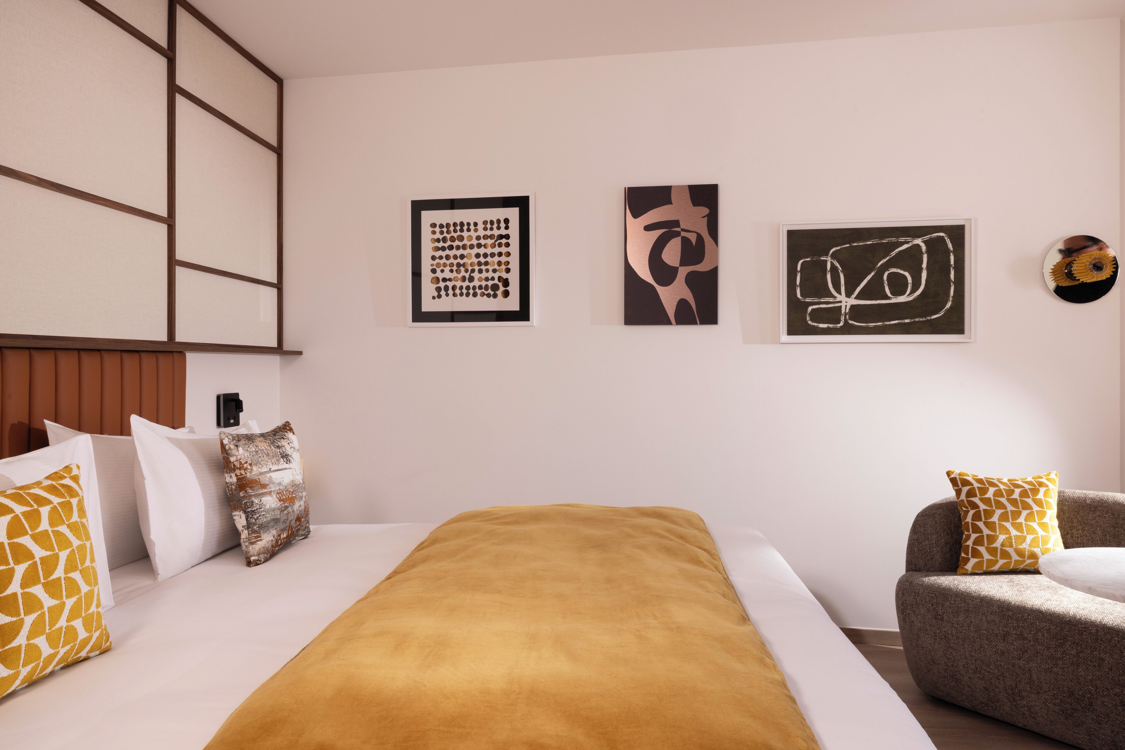 A modern hotel room with a large bed, a sofa, and three framed artworks on the wall.