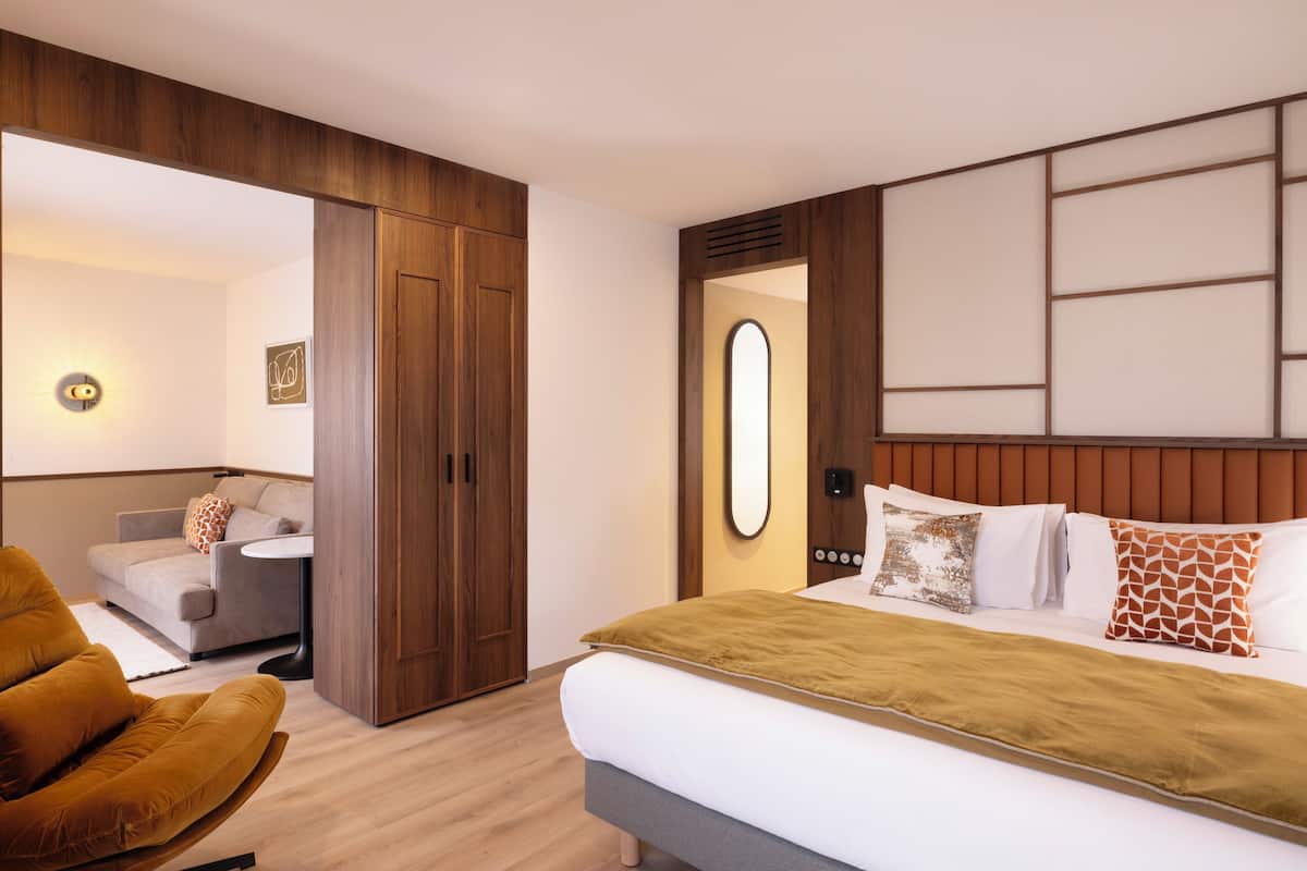 A modern hotel room with a bed, a sofa, a wooden wardrobe, and a small table.