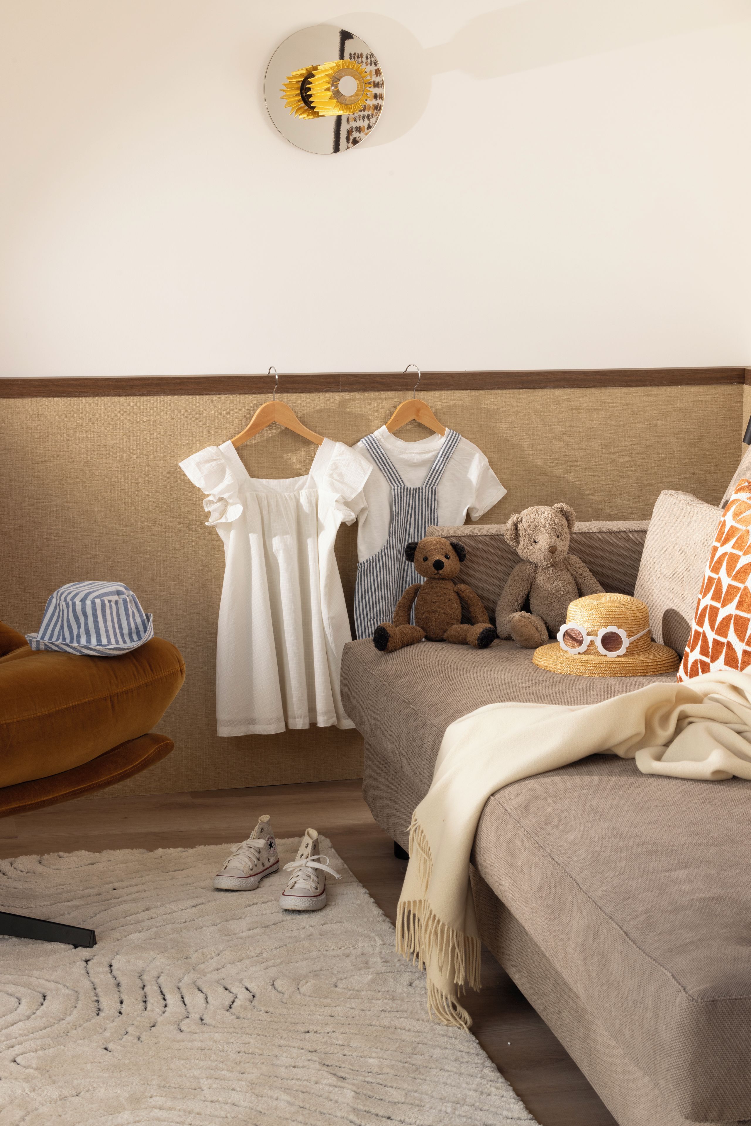 A cozy living room with a brown sofa, a wooden chair, a small rug, and children's clothing on hangers.