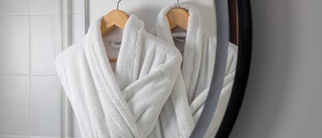 Un baño con pared de azulejos blancos, un perchero de madera y un espejo.