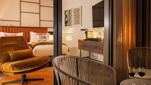 Habitación de hotel moderna con cama, sofá, silla, escritorio y dos copas de vino sobre una mesita.