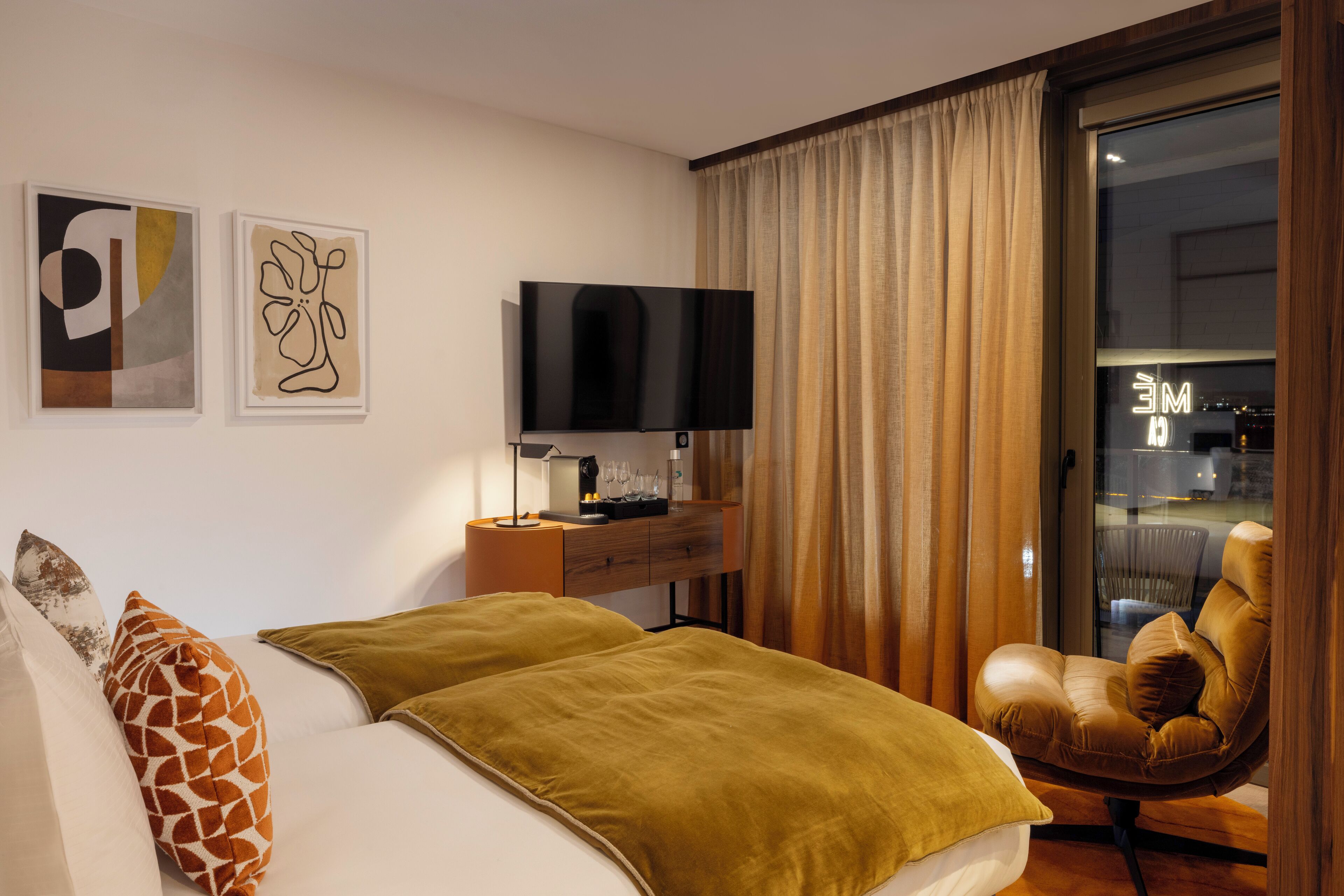 A modern hotel room with a bed, a TV, a desk with a lamp, and a chair.