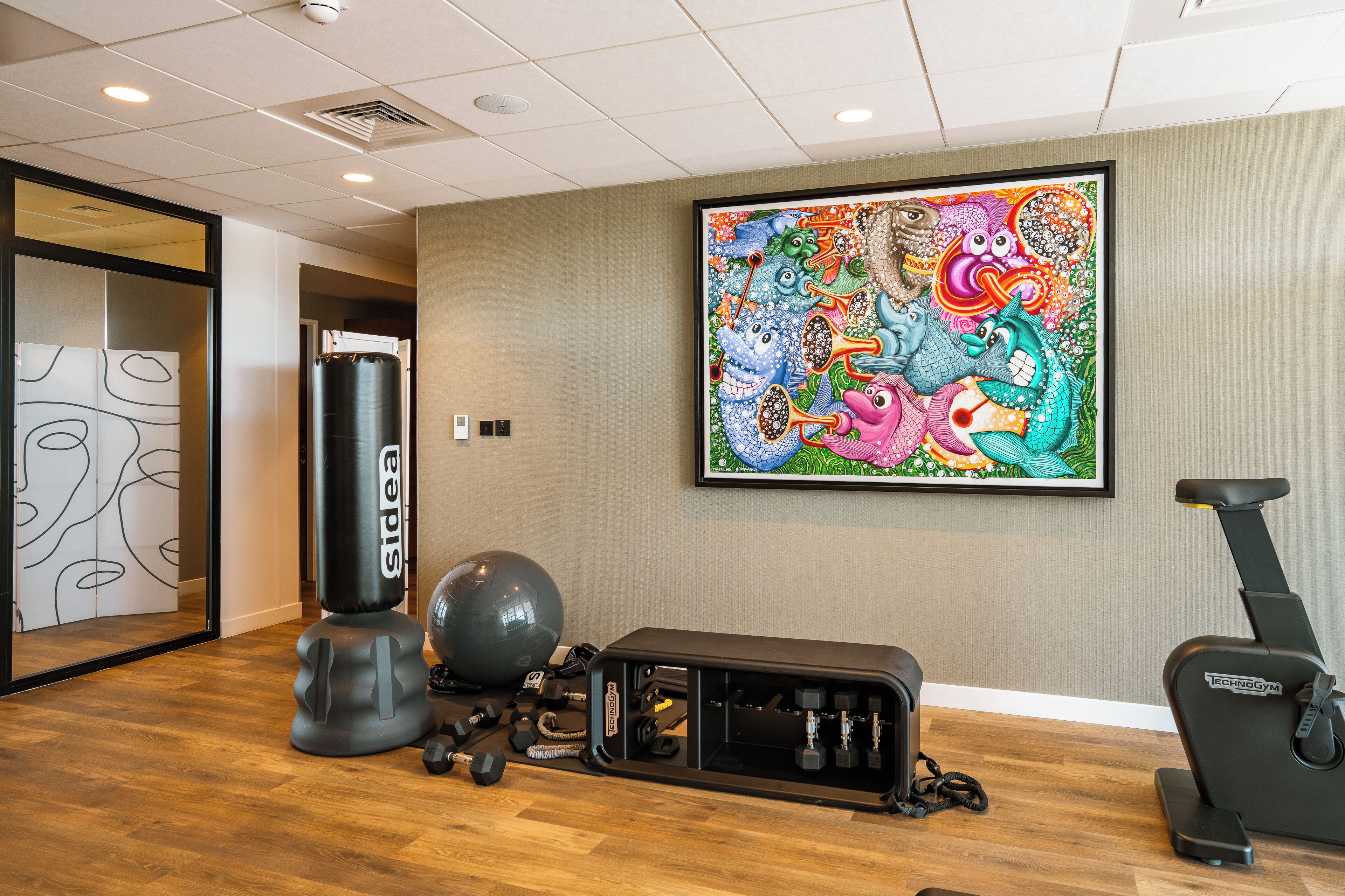 Une salle de sport équipée de matériel d’exercice, d’un sac de frappe et ornée d’une fresque murale aux couleurs vives.