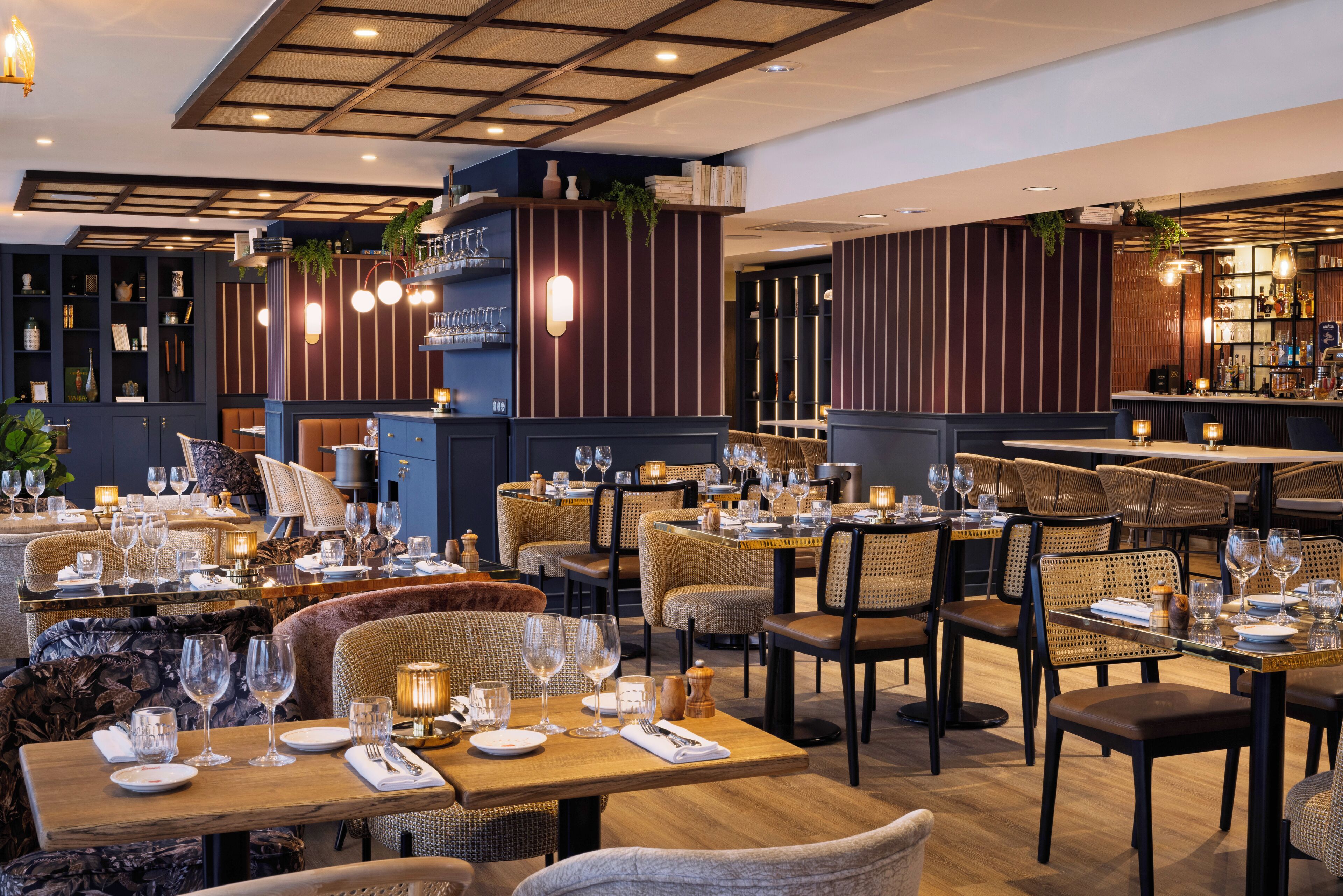 A modern restaurant with multiple dining tables and chairs, a bar area, and decorative lighting.