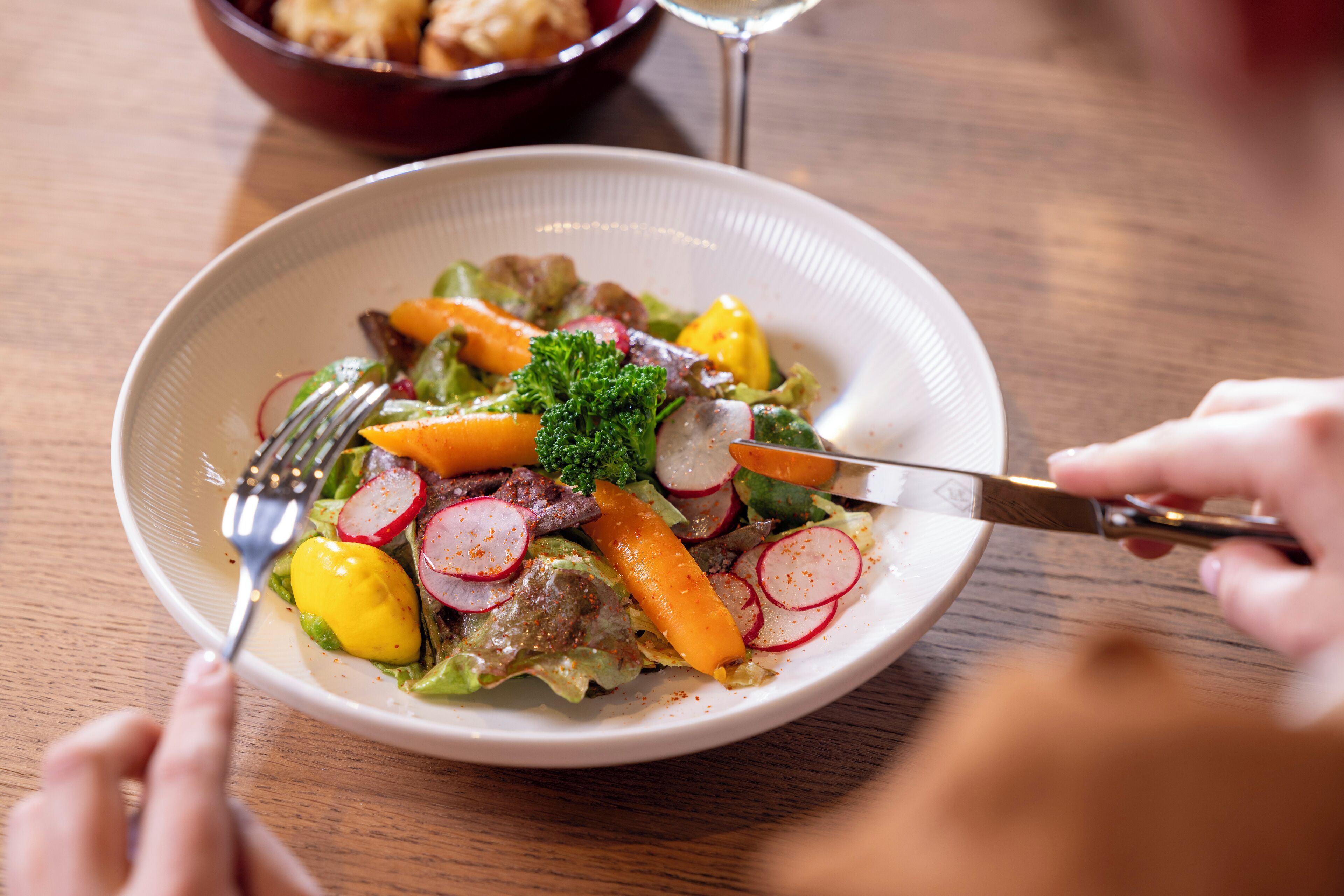 A plate of salad with various vegetables and a fork and knife on a wooden table.