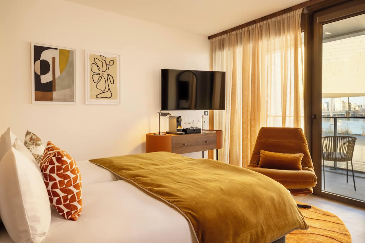 A hotel room with a bed, a TV, a desk, a chair, and a balcony with a view.
