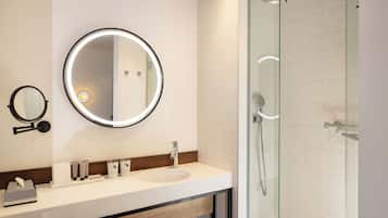 A modern bathroom with a round mirror, a sink, and a glass-enclosed shower.
