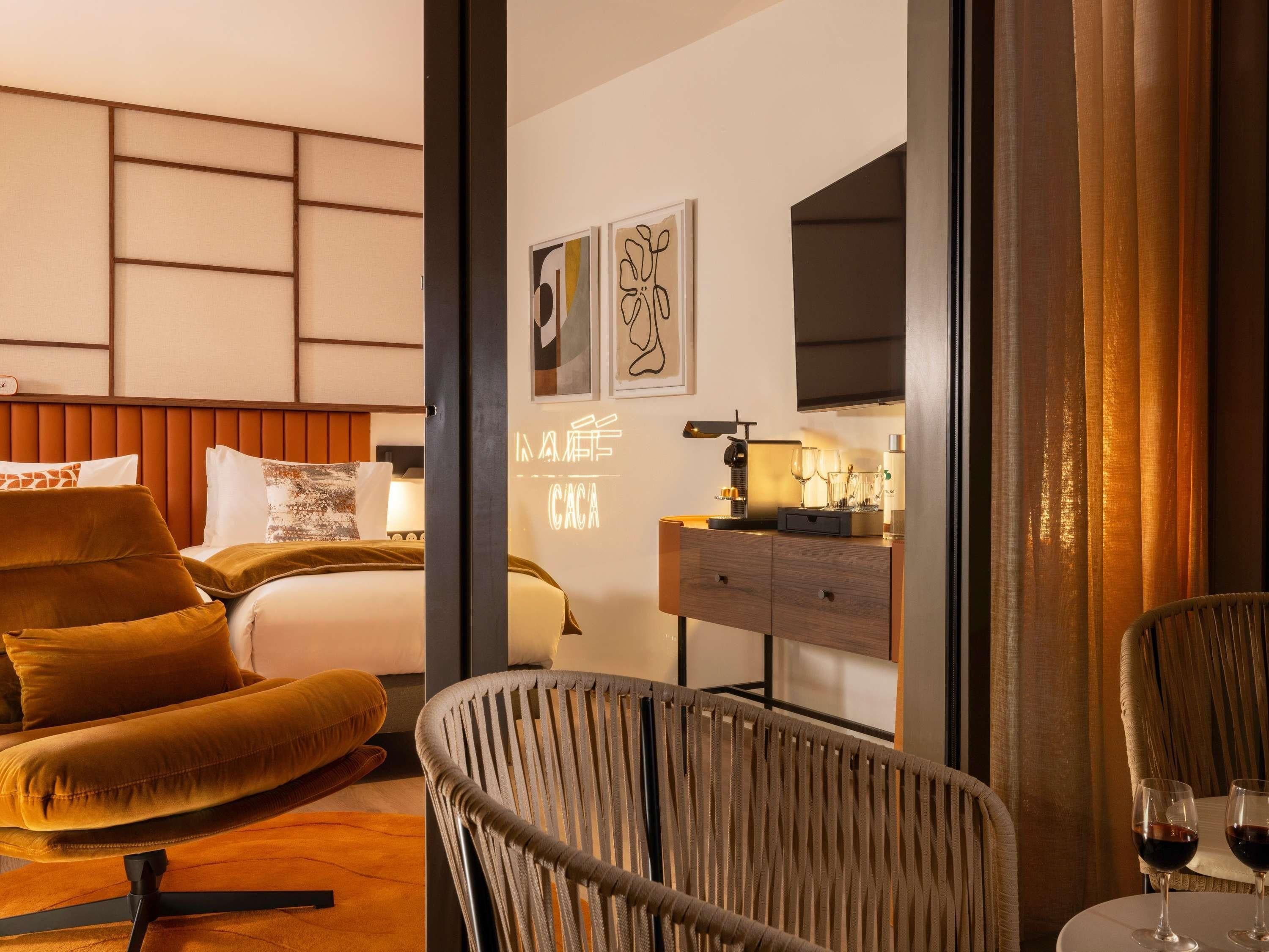 A hotel room with a bed, a sofa, a chair, a desk with a lamp, and a television.
