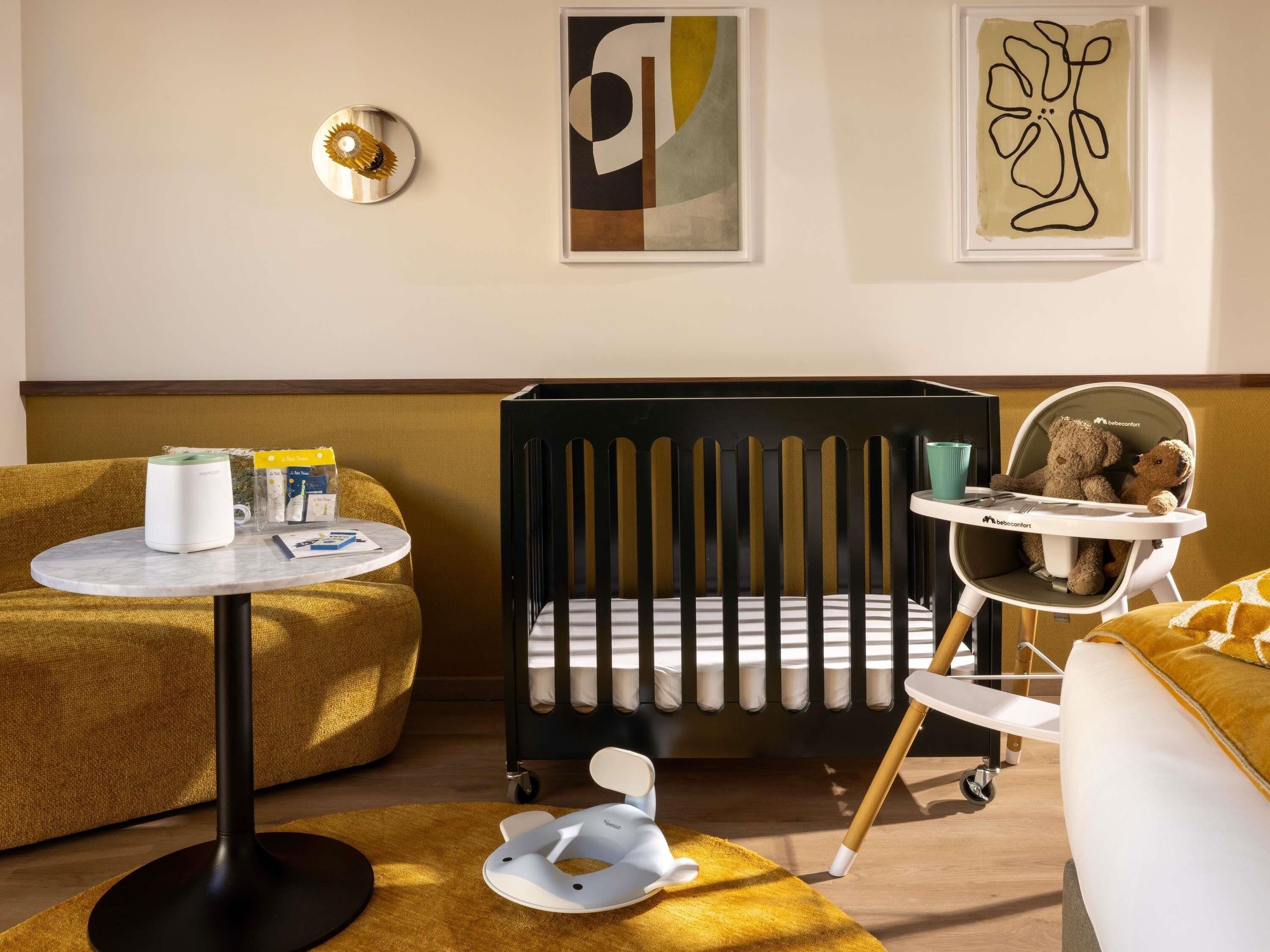Una habitación moderna para bebés con una cuna, una trona y un asiento para bebé.