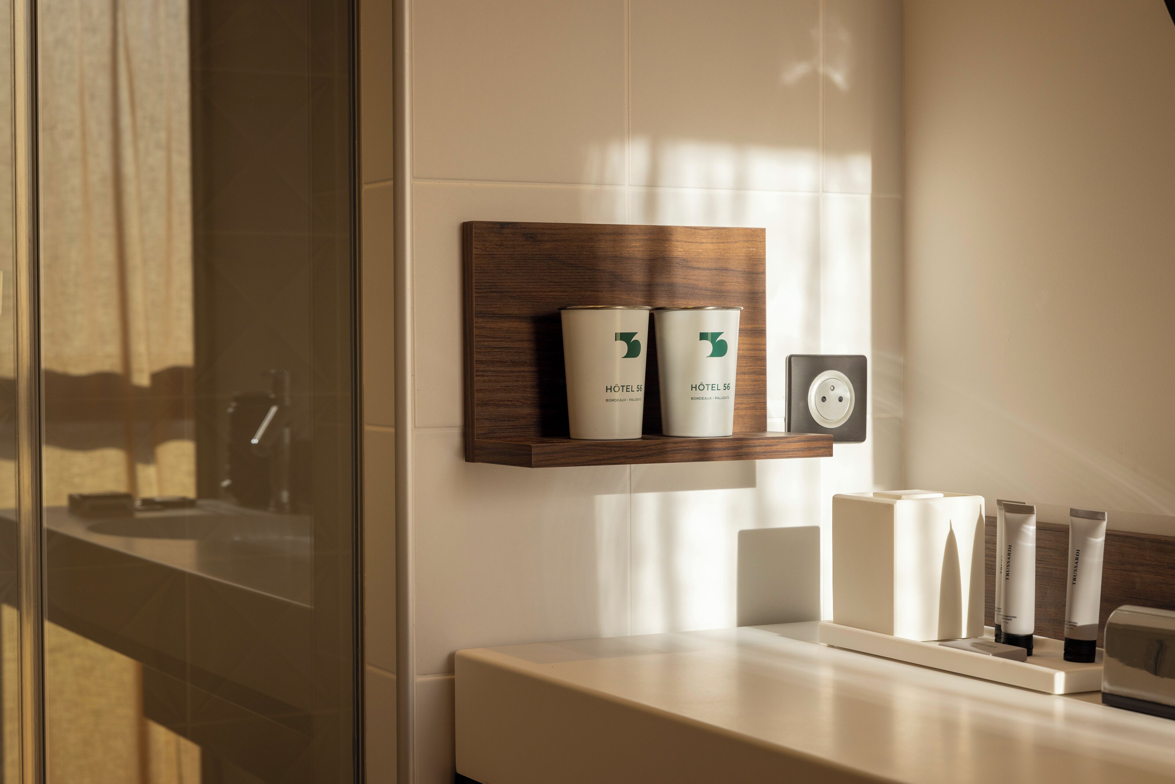 A modern bathroom with a wooden shelf holding toiletries, a mirror, and a power outlet.