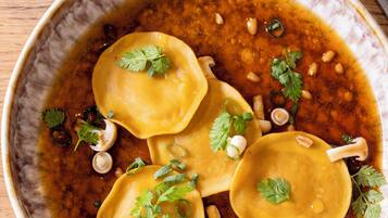A bowl of ravioli with sauce and garnishes on a wooden table.