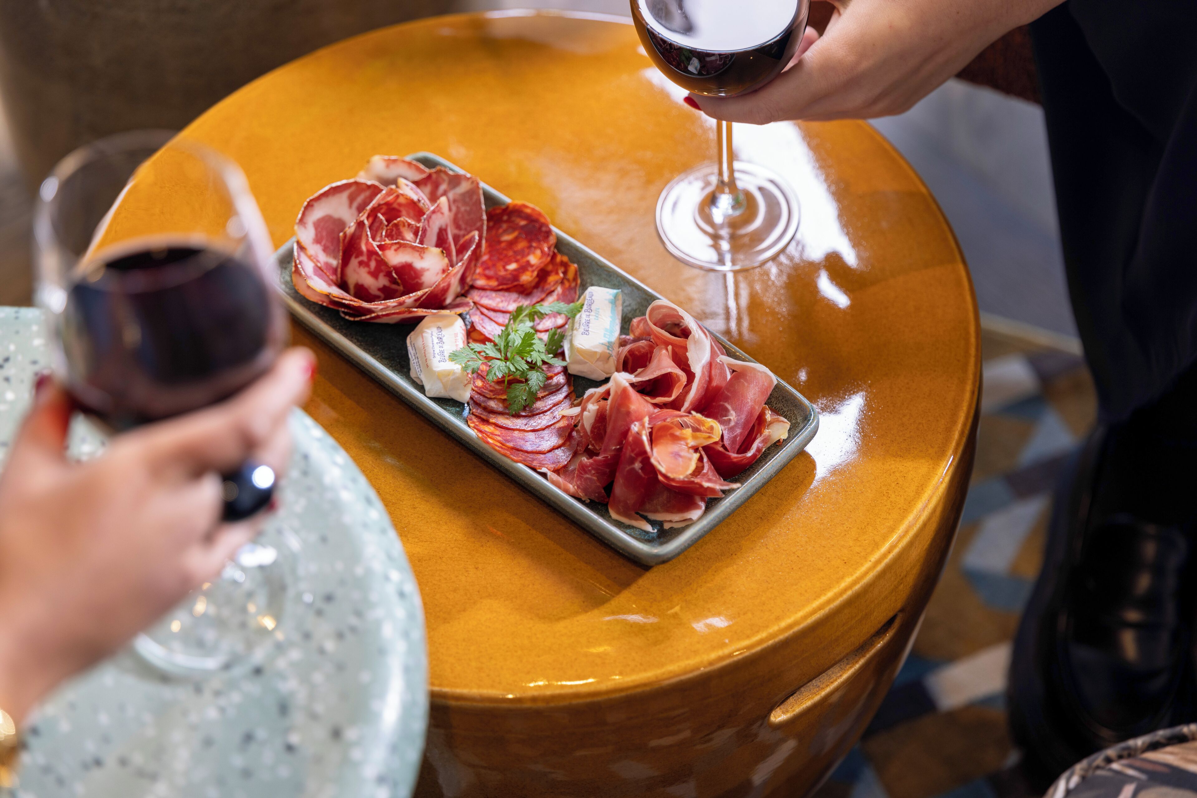 Une table avec une assiette de charcuteries et de fromages, et un verre de vin rouge.