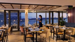 Un restaurante moderno con vistas a la ciudad, donde un camarero sirve una bandeja de copas.