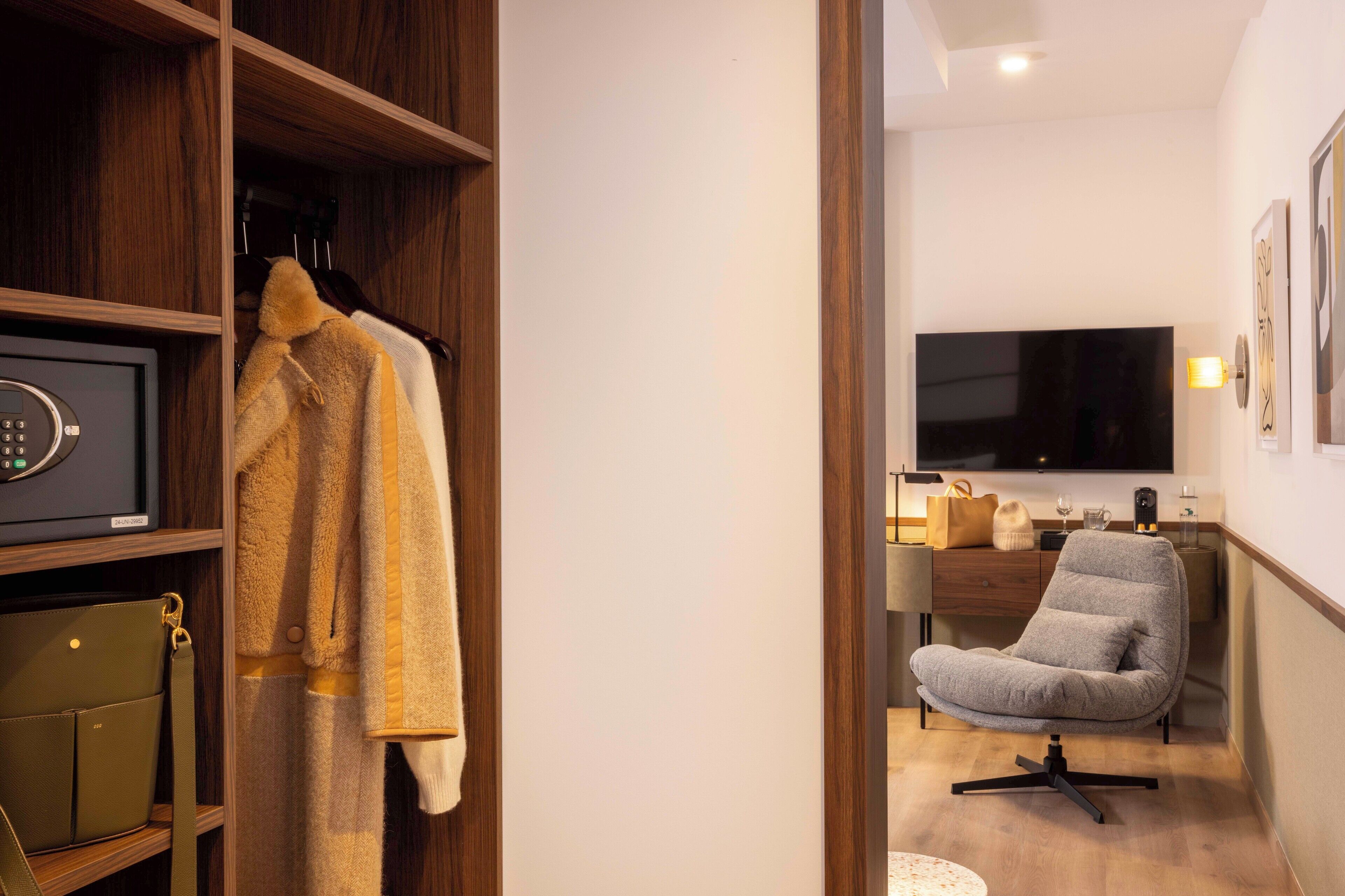 A modern room with a wooden wardrobe, a grey office chair, a TV, and a safe.