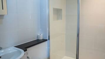 Un baño moderno con ducha de vidrio, inodoro blanco y lavamanos.