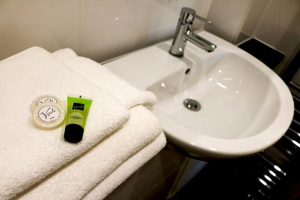 A bathroom with a white sink, a towel, and two bottles of Verdi soap.