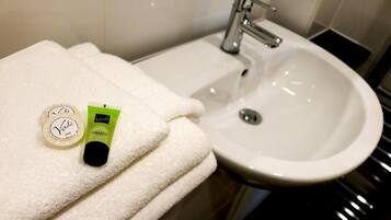 A bathroom with a white sink, a towel, and two bottles of Verdi soap.