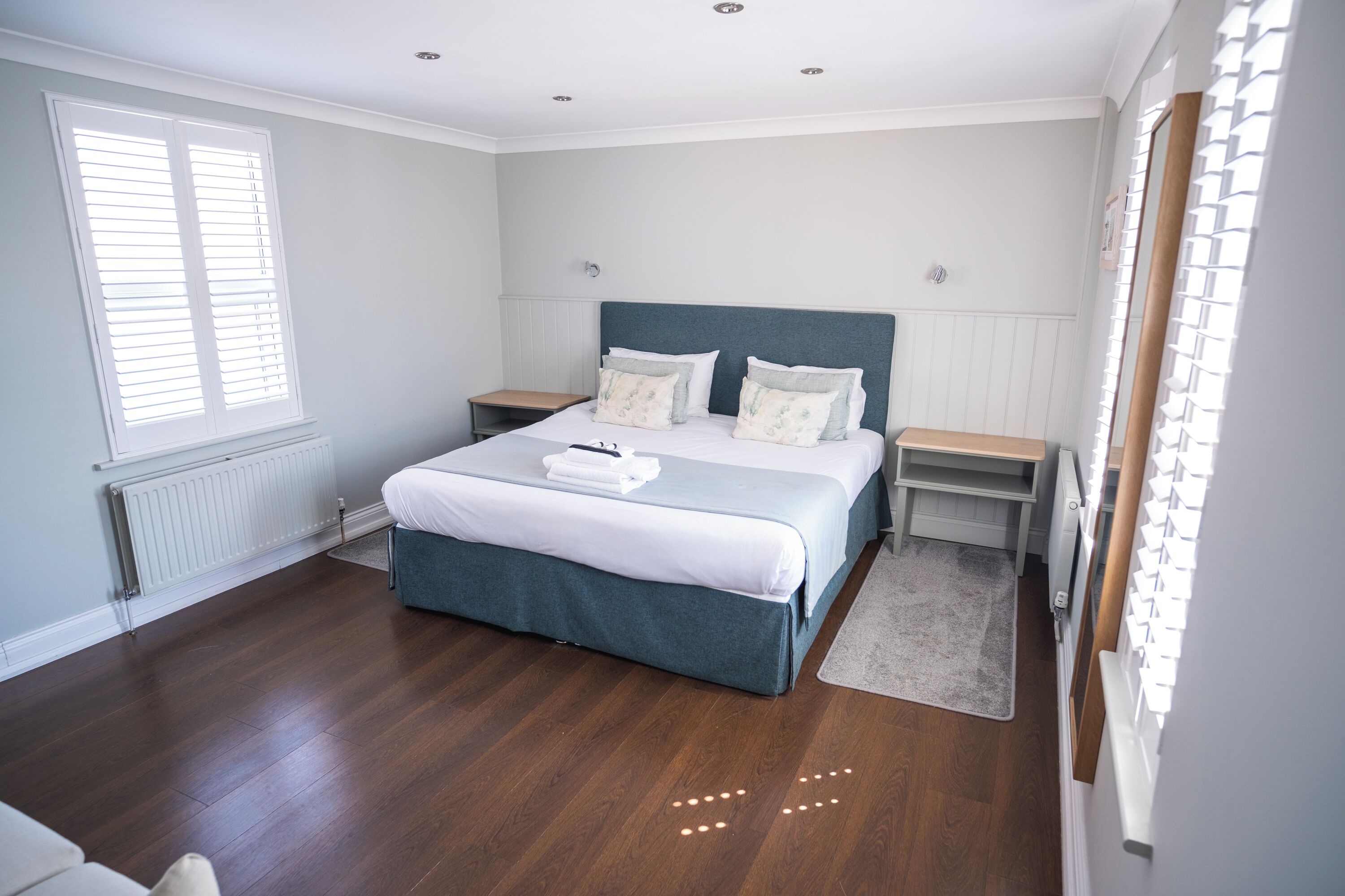 A bedroom with a large bed, two bedside tables, a window with blinds, and a radiator.