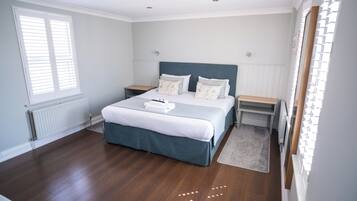 A bedroom with a large bed, two bedside tables, a window with blinds, and a radiator.