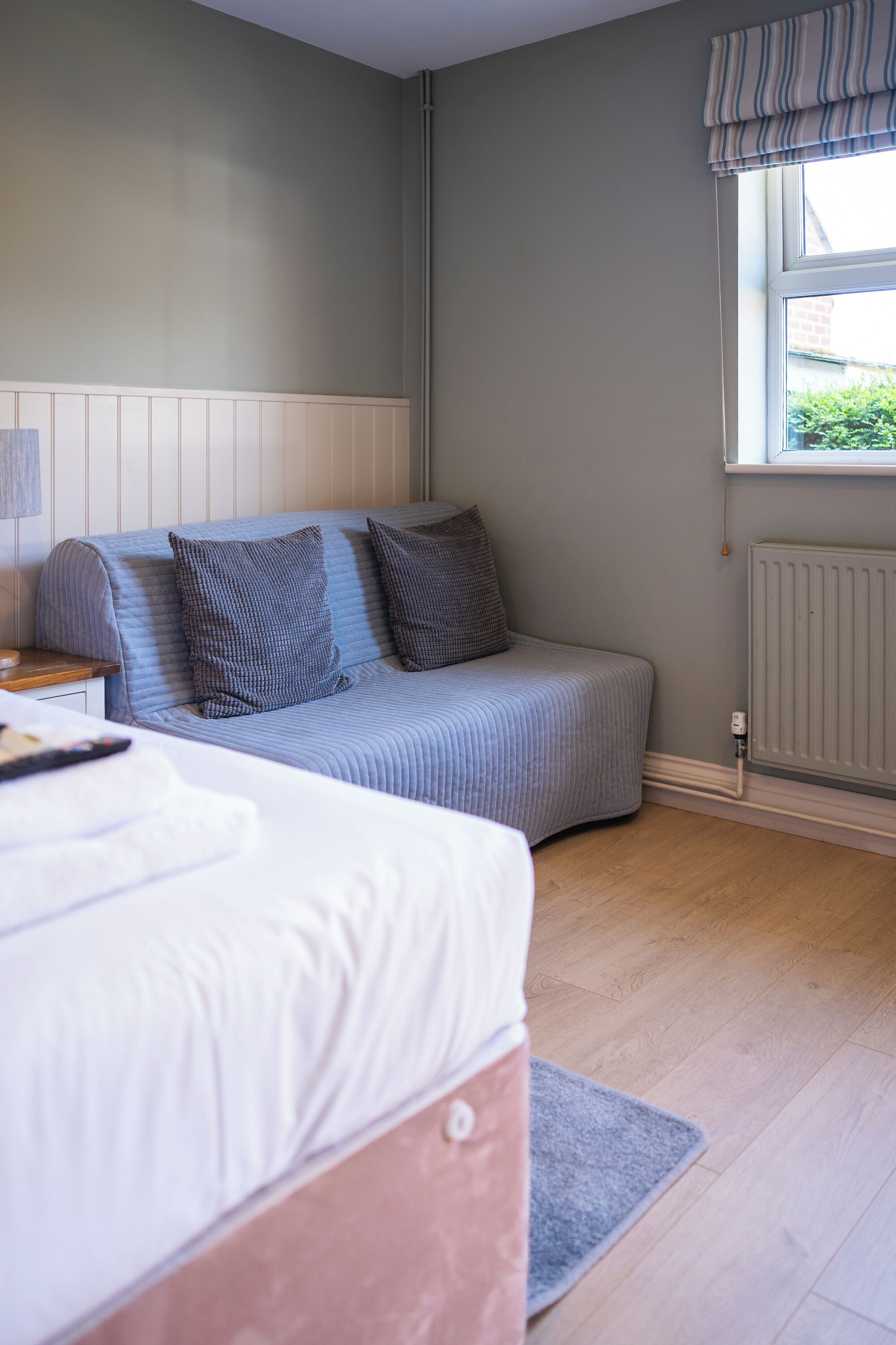 Un dormitorio con cama, sofá, radiador y ventana con cortinas.