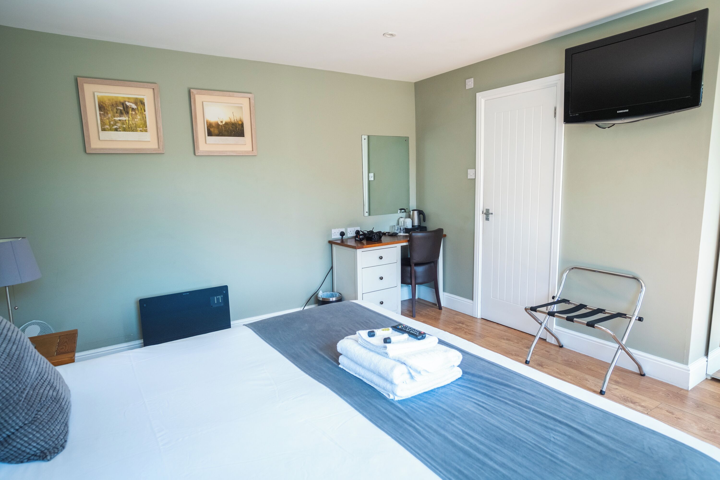 A hotel room with a bed, a desk, a chair, a television, and two framed pictures on the wall.