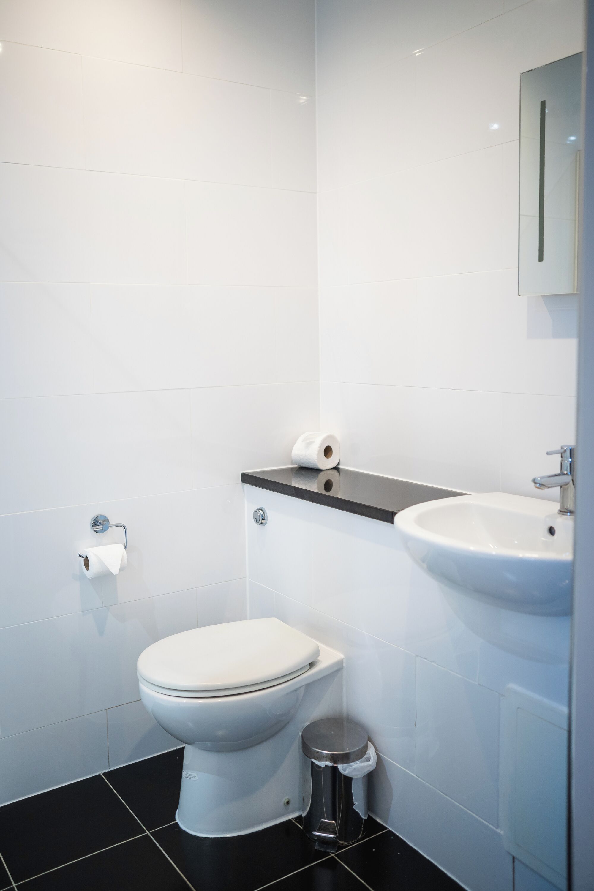 A modern bathroom with a toilet, sink, and a trash bin.